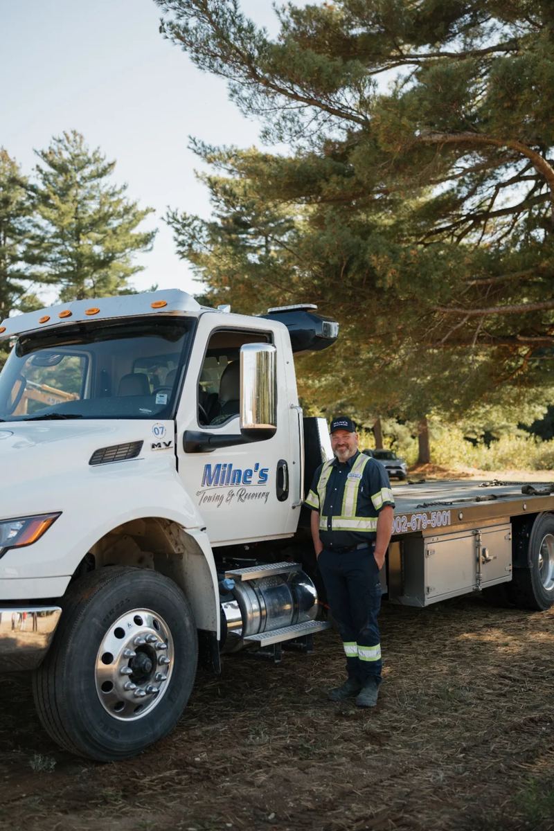 Chris beside a white Milne's flatbed, parked in front of the pines.