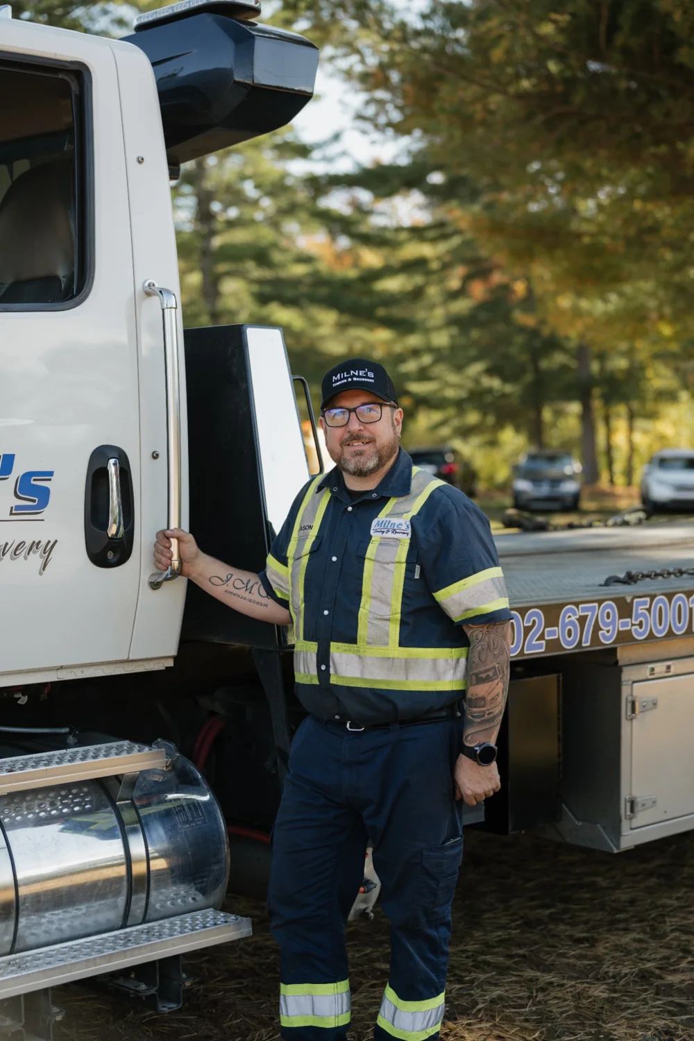 Jason, in glasses and a Milne's cap, with one hand on the grab handle of a Milne's flatbed.