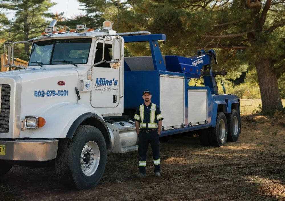 Milne's blue and white heavy wrecker, unit 01, with the Milne's name on the door, the phone number on the hood and a crew member beside it.